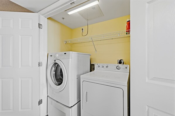 Une buanderie équipée d’un lave-linge et d’un sèche-linge, avec une porte blanche et un mur jaune.