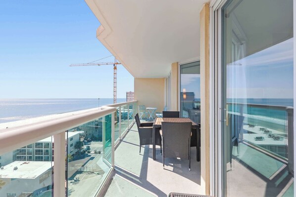 A balcony with a table and chairs, overlooking a construction site and the sea.