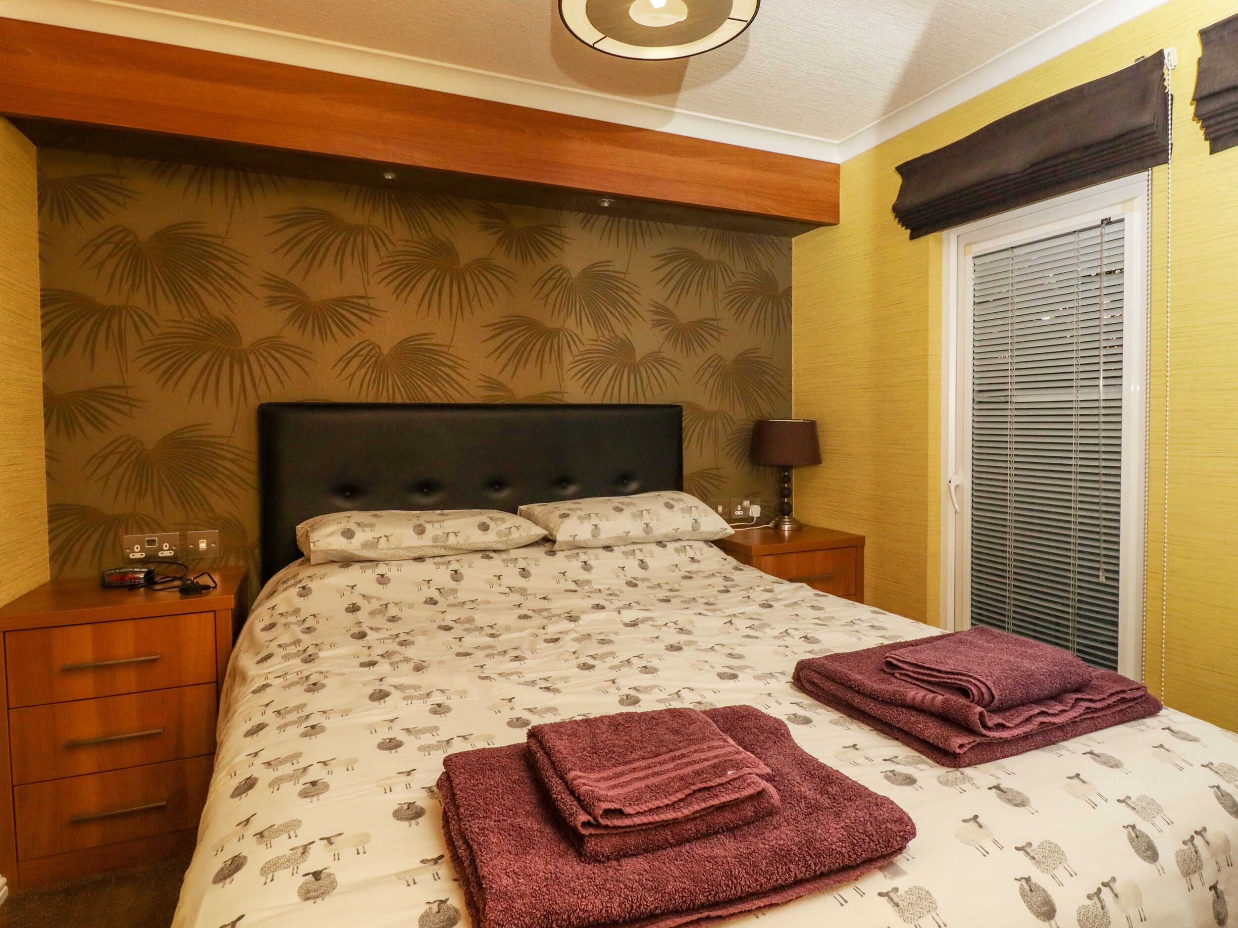 A bedroom with a bed, nightstands, a lamp, and a window with blinds.