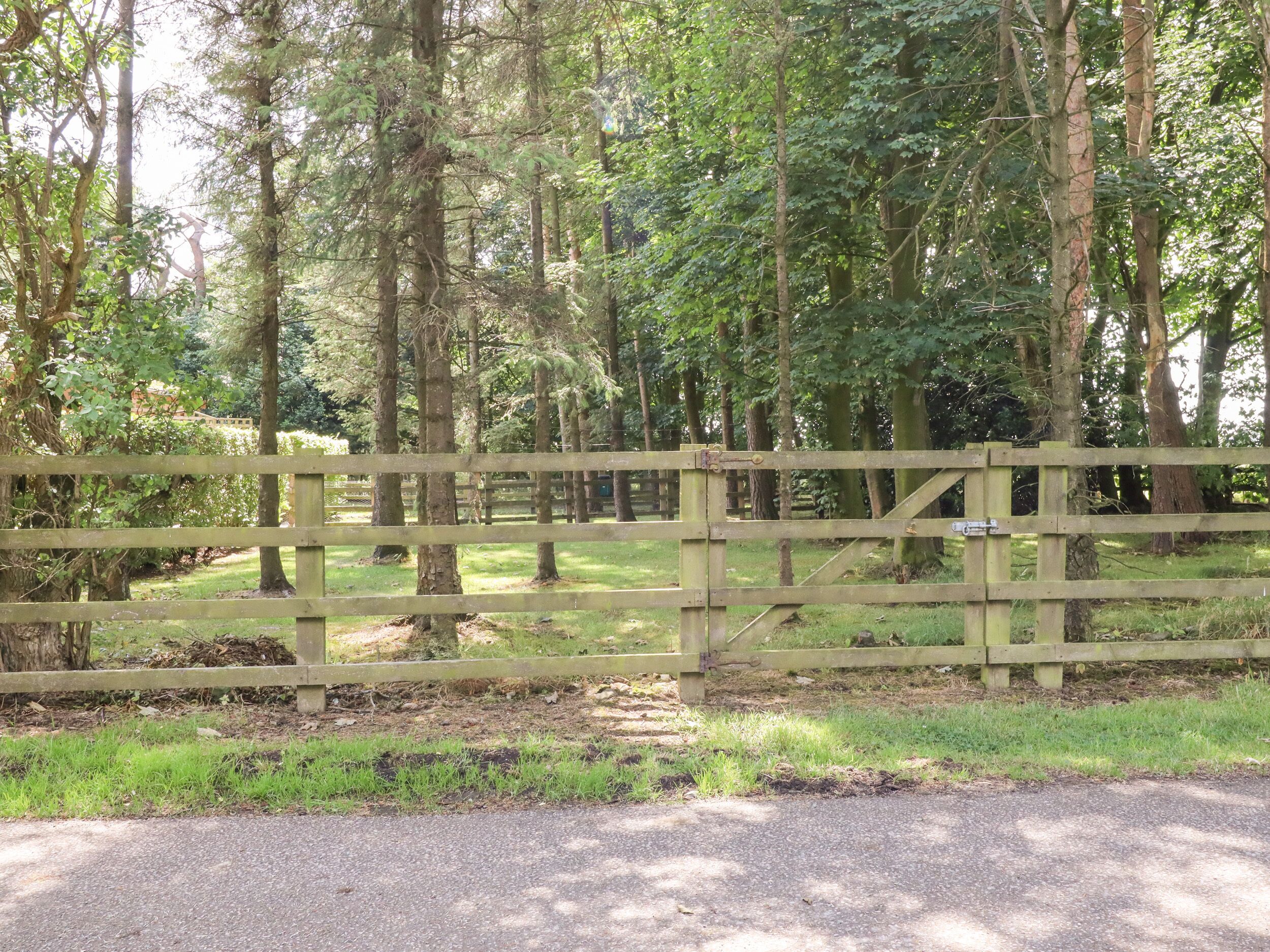 A wooden gate in a forested area with a paved path leading through it.