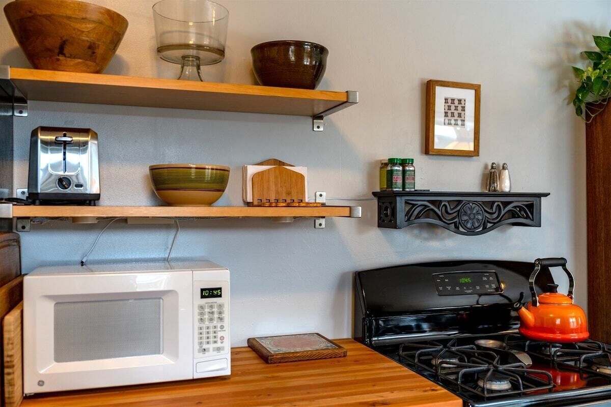 Een keuken met een witte magnetron, een fornuis en houten planken met verschillende keukenspullen.