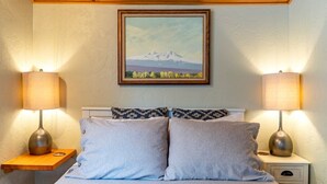 A bedroom with a bed, two bedside lamps, a nightstand, a drawer, and a framed picture of a mountain on the wall. - Bluebird Day - Desert Moon, Cozy 2BR in Bend's River West, Walkable to restaurants! (Bend)