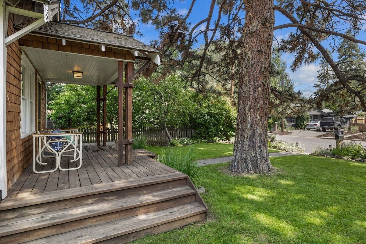 A wooden deck with steps leading to a covered porch, surrounded by a well-maintained lawn and large trees.