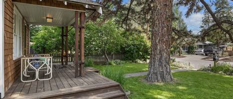 A wooden deck with steps leading to a covered porch, surrounded by a well-maintained lawn and large trees.