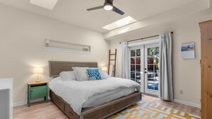 A bedroom with a bed, a nightstand, a ceiling fan, a window with curtains, and a view of the outdoors. - Bluebird Day - Hartford Haven, a spacious 3BR home with modern amenities. (Bend)