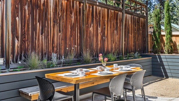 An outdoor dining area with a wooden table and chairs, a decorative vase with flowers, and a wooden fence in the background. - Bluebird Day - Hartford Haven, a spacious 3BR home with modern amenities. (Bend)