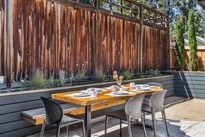 An outdoor dining area with a wooden table and chairs, a decorative vase with flowers, and a wooden fence in the background. - Bluebird Day - Hartford Haven, a spacious 3BR home with modern amenities. (Bend)