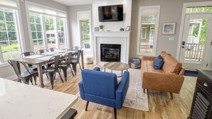 A spacious living room with a fireplace, a television mounted above it, and a dining area with a table and chairs. - 6 bed in Beachwalk Resort w/Pool, Lake, Golf Cart (Michigan City)