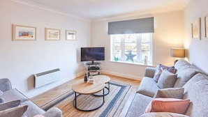 A modern living room with a sofa, a coffee table, a TV, and framed pictures on the wall. - Host & Stay | Harbour View (Whitby)