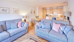A modern living room with two grey sofas, a dining table, and a kitchen in the background. - Host & Stay | Harbour View (Whitby)