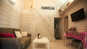 Un salon confortable avec un canapé, une petite table blanche, un téléviseur fixé au mur et un escalier menant à un autre niveau.