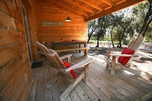 A wooden cabin with a covered porch, a bench, and two rocking chairs.