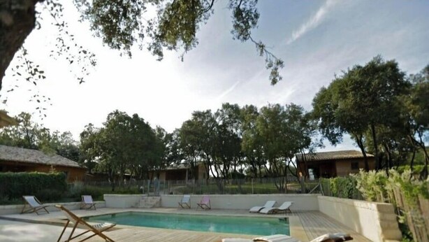 Une terrasse en bois avec des chaises longues et une piscine, entourée d’arbres et d’immeubles.