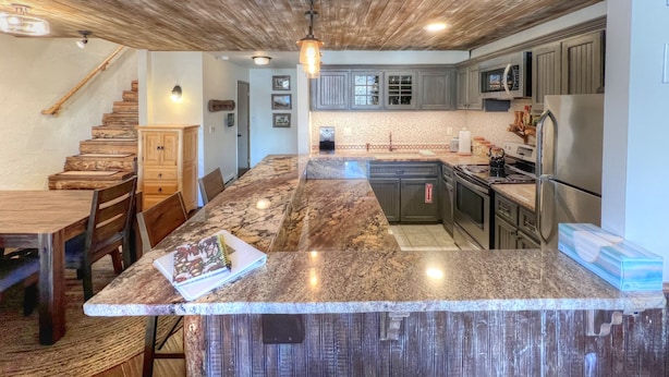 A kitchen with a wooden ceiling, granite countertops, and stainless steel appliances.