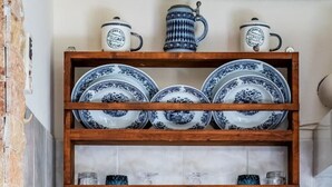 A kitchen with a wooden shelf holding blue and white plates and cups, a stainless steel sink, and a wooden cabinet. - Cottage Cozy Studio (Yianna Cottage Studios) (Skopelos)