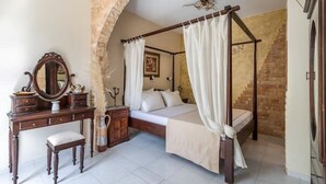 A four-poster bed with white curtains, a wooden dresser with a mirror, and a stone archway. - Cottage Cozy Studio (Yianna Cottage Studios) (Skopelos)