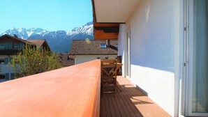 A wooden deck with a table and chairs, overlooking a mountain range. - Comfortable, bright vacation apartment with balcony and alpine view in Pfronten Mitte (Pfronten)