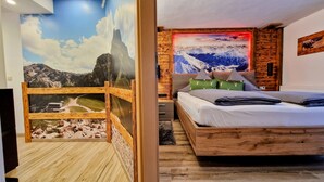 A bedroom with a wooden bed, a nightstand, a wall-mounted TV, and a mural of a mountainous landscape. - Comfortable, bright vacation apartment with balcony and alpine view in Pfronten Mitte (Pfronten)
