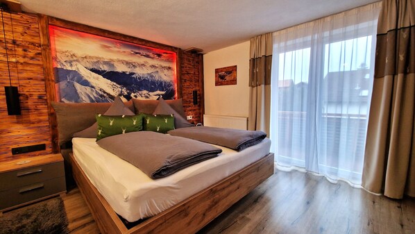 A bedroom with a wooden bed frame, a mountain landscape mural, and a window with sheer curtains.