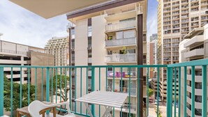 A balcony with a table and chairs, overlooking a residential area with multi-story buildings.