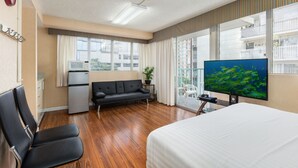 A hotel room with a bed, a sofa, a TV, a desk, and a balcony with a view of buildings.