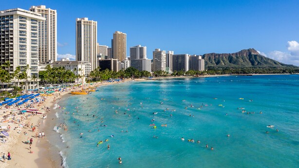 A beach with clear turquoise waters, a sandy shore, and a city skyline with tall buildings in the background.
