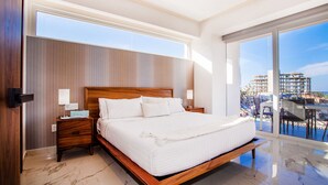 A modern bedroom with a large bed, wooden headboard, and a view of a cityscape through large windows.