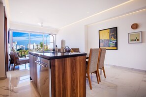Une cuisine moderne dotée d’un grand îlot central, d’un coin repas avec des chaises et offrant une vue sur la ville grâce à de grandes fenêtres.
