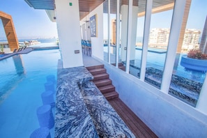 A modern poolside area with a marble-tiled bench, wooden steps, and a view of the sea. - Luxe 2BR w/ Balcony, Pool & Gym (Puerto Vallarta)