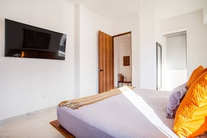 A modern bedroom with a bed, a television mounted on the wall, and a wooden door leading to another room. - Luxe 2BR w/ Balcony, Pool & Gym (Puerto Vallarta)