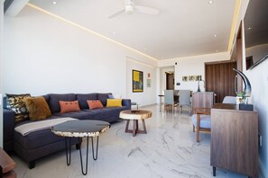 Ein modernes Wohnzimmer mit einer Couch, einem Couchtisch und Sesseln, ein Essbereich mit einem Holztisch und Stühlen sowie ein Deckenventilator.