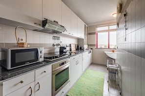 Une cuisine moderne avec des meubles blancs, un four à micro-ondes, une cuisinière, un four et un tapis vert.