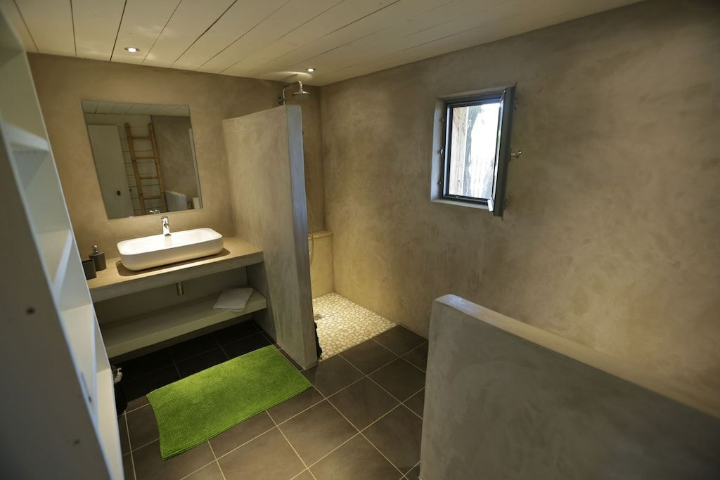 A bathroom with a sink, mirror, shower, and a small window.