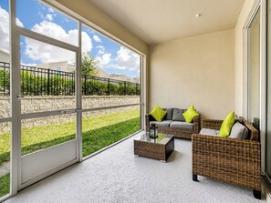 A balcony with wicker furniture, a glass door, and a view of a green landscape.