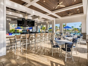 An outdoor patio area with multiple seating arrangements, including bar stools and tables, and a pool visible in the background. - Fairy Tale Disney Stay / Garage Access / Water Fun (Four Corners)