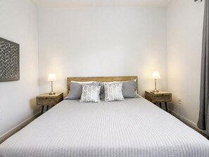 Cama bem arrumada com cabeceira, duas mesas de cabeceira com abajures e um objeto decorativo fixado na parede.
