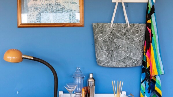 A room with a blue wall, a framed picture, a patterned bag, a lamp, a cocktail shaker, and a colorful towel. - Treetops Haven Venus Bay (Venus Bay)