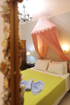 A hotel room with a bed, a nightstand, a lamp, a chandelier, and a canopy bed. - Apartment with Terrace (Yianna Cottage Studios) (Skopelos)