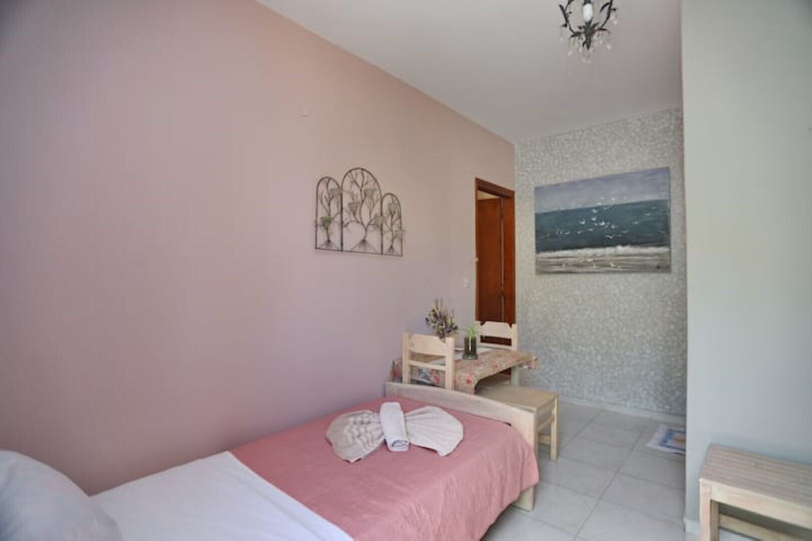 A bedroom with a bed, a desk, and a chair. There is a painting on the wall and a chandelier.