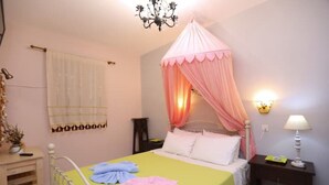 A bedroom with a bed, a nightstand, a lamp, a chandelier, and a curtain. - Apartment with Terrace (Yianna Cottage Studios) (Skopelos)