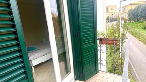 Ett rum med en skjutdörr i glas, en säng och en liten balkong med utsikt över gatan och grönområden.