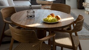 Un salon moderne avec une table à manger en bois, des chaises en osier et une vue sur la mer par une grande fenêtre.