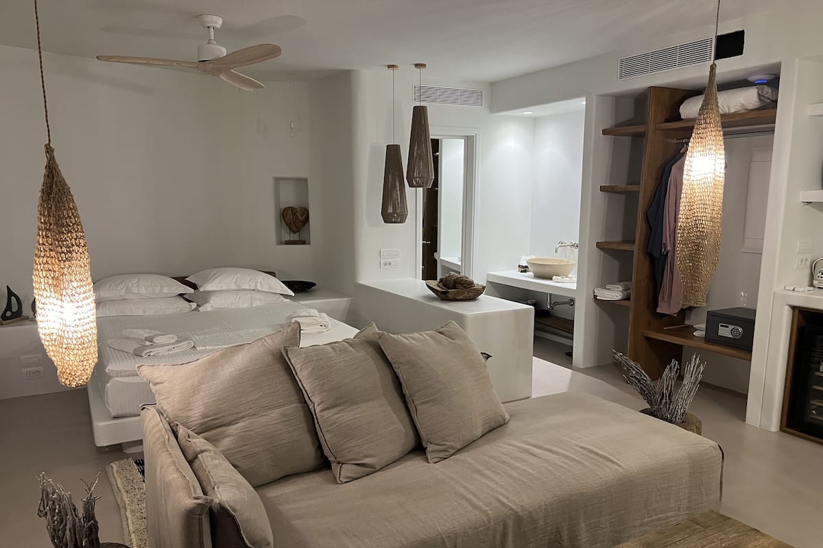 Une chambre moderne avec un lit, un canapé, une table de chevet en bois et un luminaire suspendu.