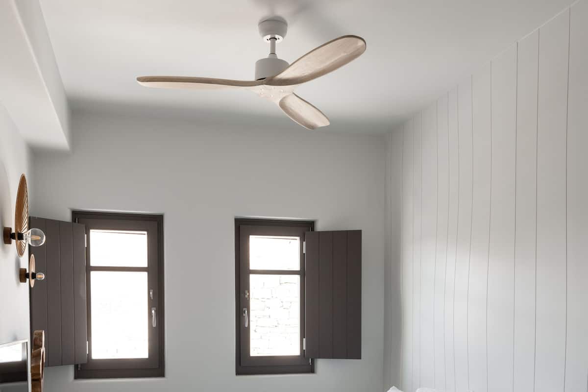 Une chambre moderne avec un grand lit, deux fenêtres, un ventilateur de plafond et une table de chevet en bois.