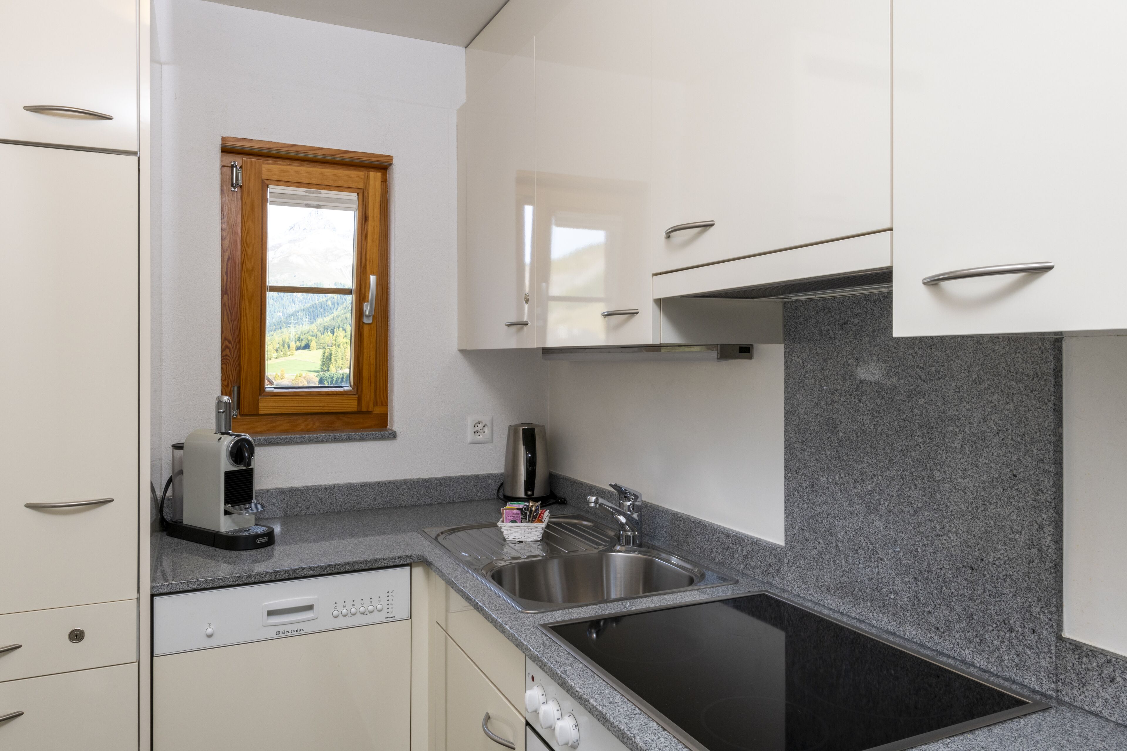 A modern kitchen with white cabinets, a granite countertop, a built-in stove, and a window with a view of mountains.
