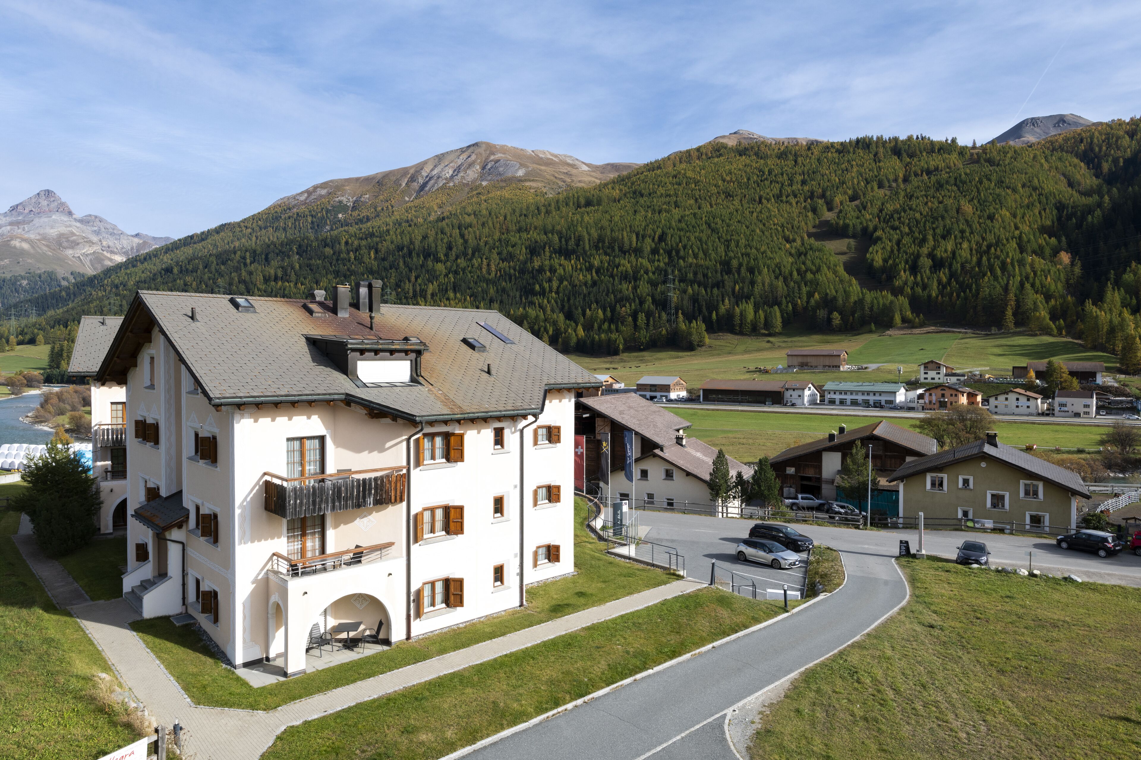 Ein mehrstöckiges Gebäude mit Balkon, Parkplatz und Blick auf eine Berglandschaft.