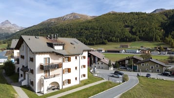 Ein mehrstöckiges Gebäude mit Balkon, Parkplatz und Blick auf eine Berglandschaft.
