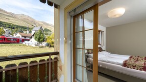 Un dormitorio con un ventanal grande, una cama y vistas a trenes y casas a lo lejos.