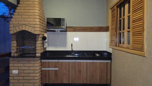 A compact kitchen with a brick fireplace, a microwave, and wooden cabinets. - Alto Costa Flats (Olímpia)