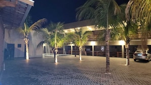 A paved courtyard with palm trees and a building with illuminated windows. - Alto Costa Flats (Olímpia)